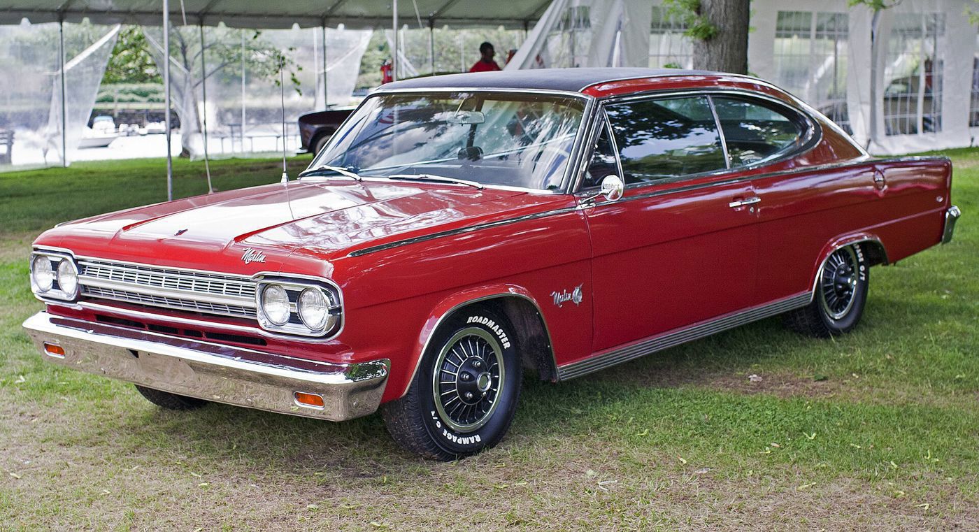 Red 1966 Rambler Marlin fastback with a black roof and turbine wheel covers, front three-quarter on grass