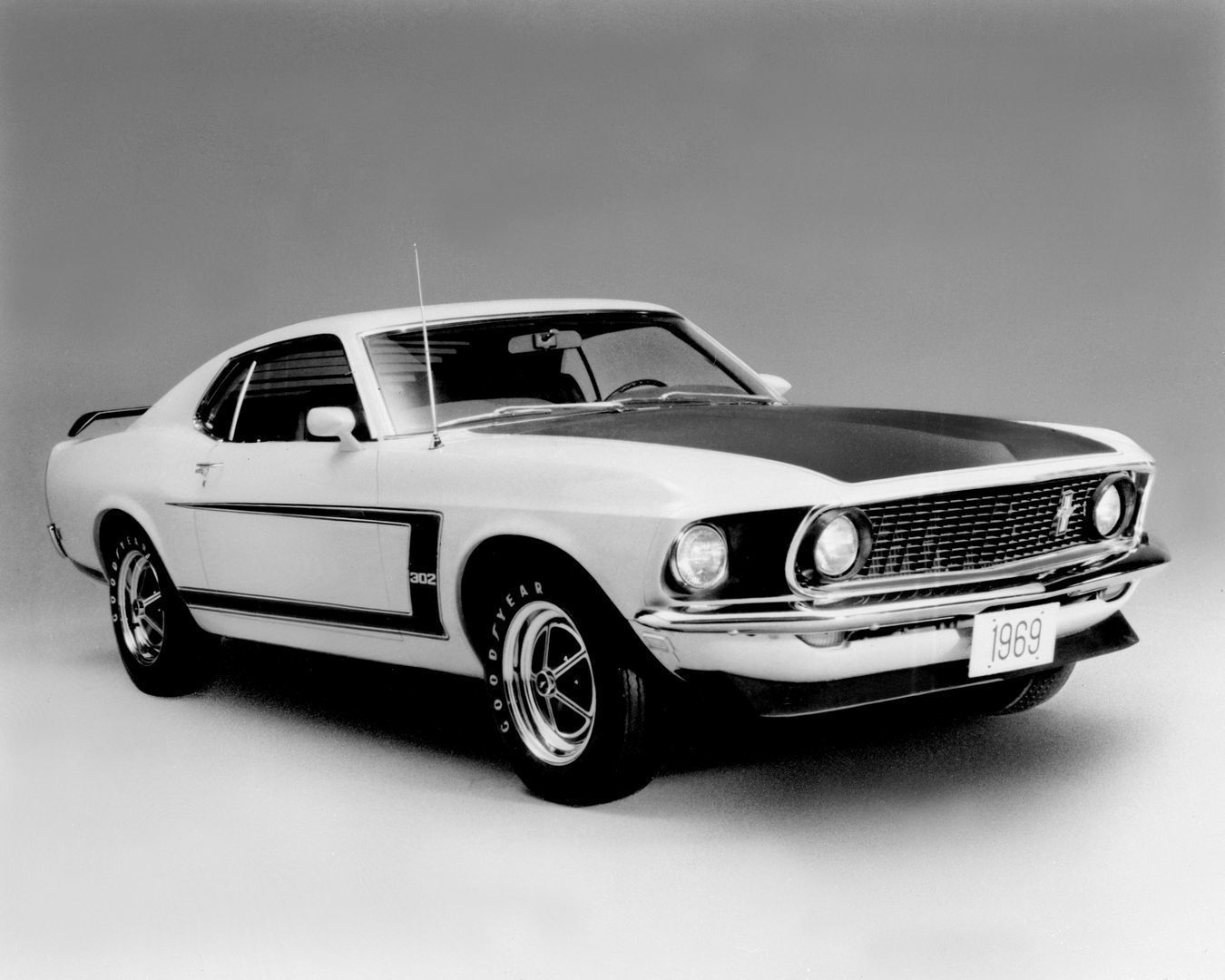 Black-and-white studio photograph of a 1969 Mustang Boss 302 with blacked-out hood, reflective C-stripe with 302 lettering and a 1969 display plate