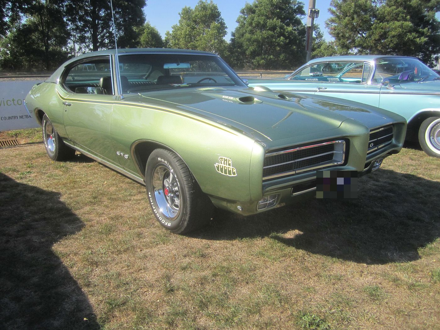 Green 1969 Pontiac GTO Judge hardtop with The Judge decal on the front fender and Endura nose, front three-quarter on grass