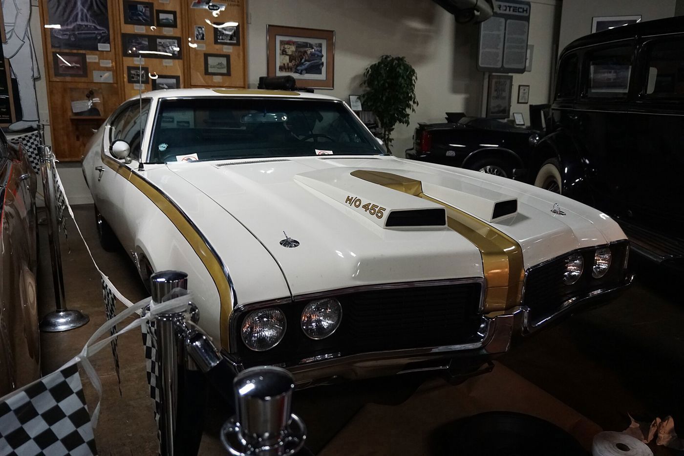 White 1969 Hurst/Olds with gold stripes and the H/O 455 twin-snorkel hood scoop, front view in a museum