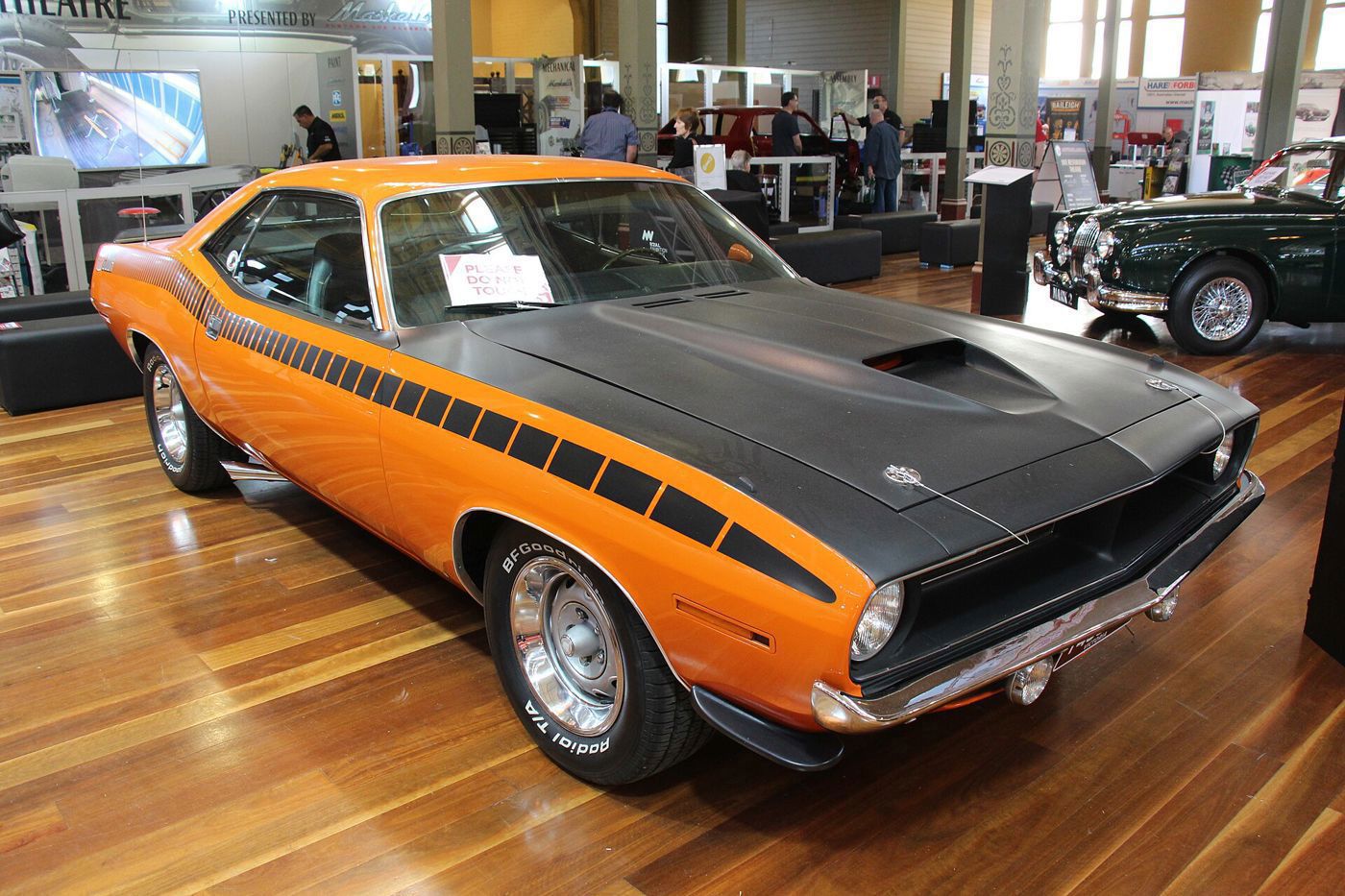 Orange 1970 Plymouth AAR Cuda with a matte black hood and strobe side stripe, displayed indoors