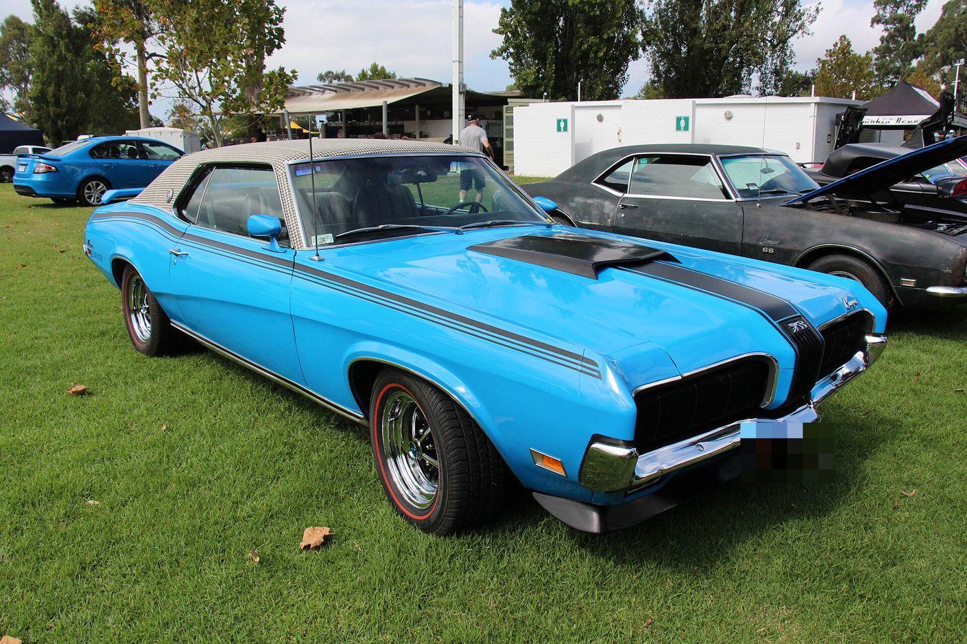 Bright blue 1970 Mercury Cougar Eliminator with black side stripes, hood scoop and houndstooth vinyl roof, front three-quarter on grass