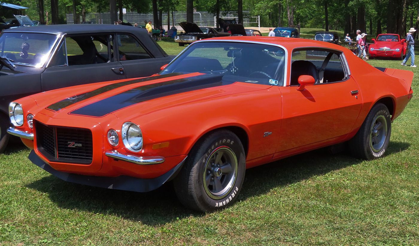 Orange 1971 Camaro Z28 with black stripes, split Rally Sport bumpers and rear spoiler, front three-quarter on grass