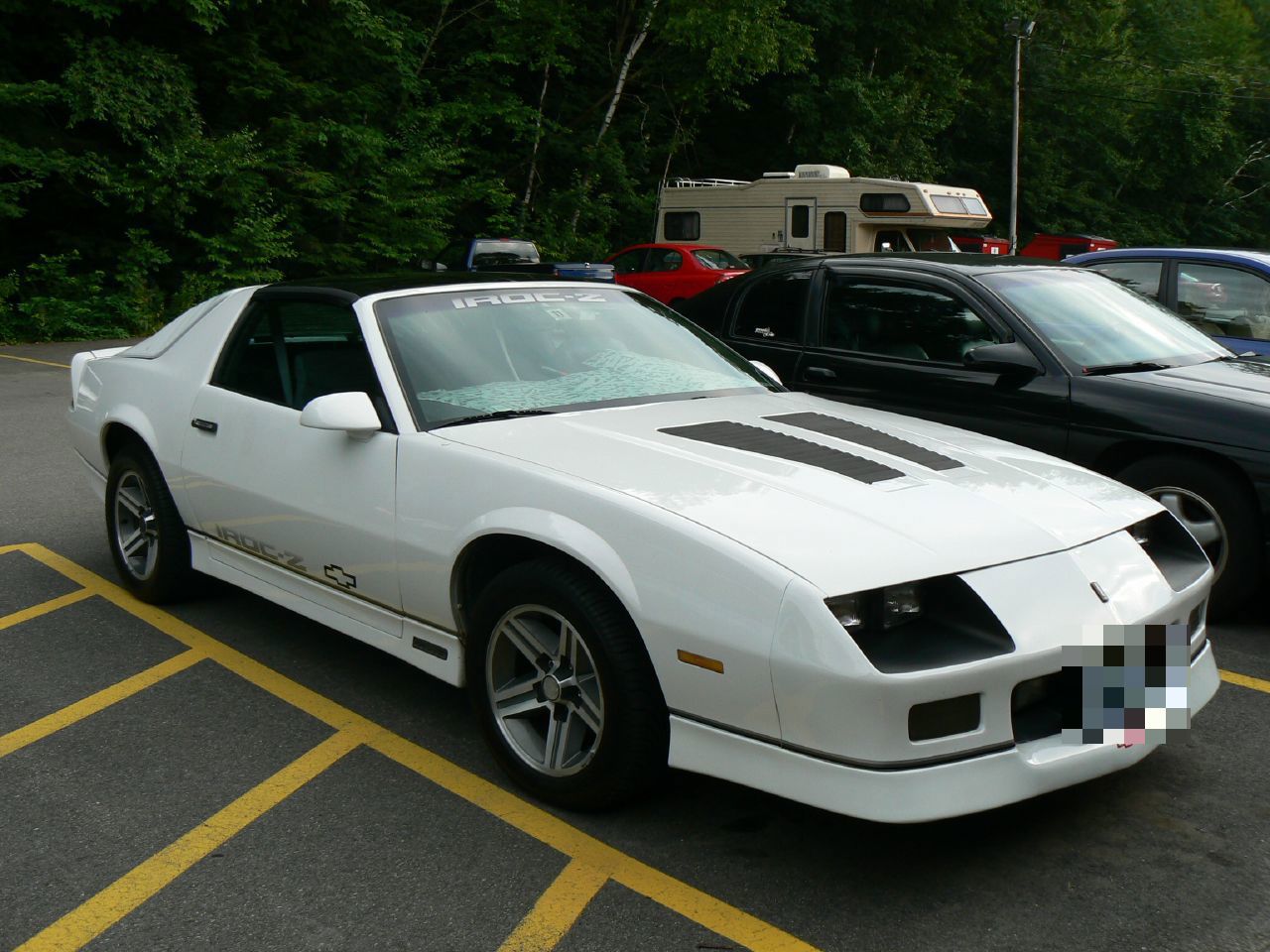 White 1987 Camaro IROC-Z with windshield banner and hood louvers, front three-quarter in a parking lot