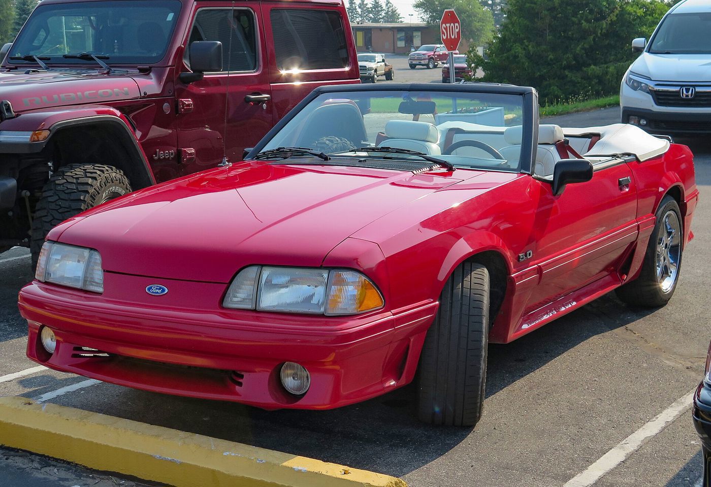 Red 1991 Ford Mustang GT convertible with the top down and 5.0 fender badge, front three-quarter in a parking lot