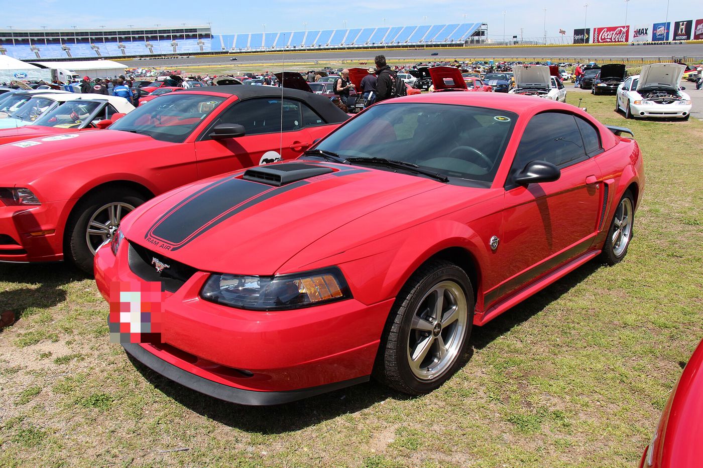 Red 2003-2004 Mustang Mach 1 with black hood stripe and Shaker scoop, front three-quarter at a speedway car show