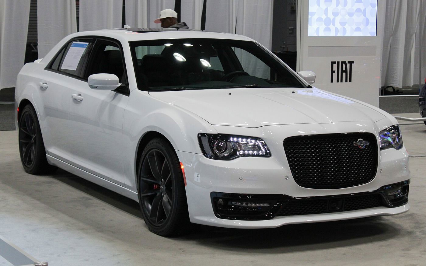 White 2023 Chrysler 300C with black mesh grille and black wheels on an auto show floor