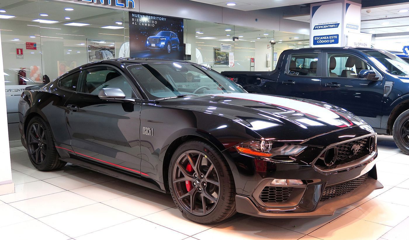 Black S550 Mustang Mach 1 with orange accent stripe and Mach 1 fender badge in a showroom