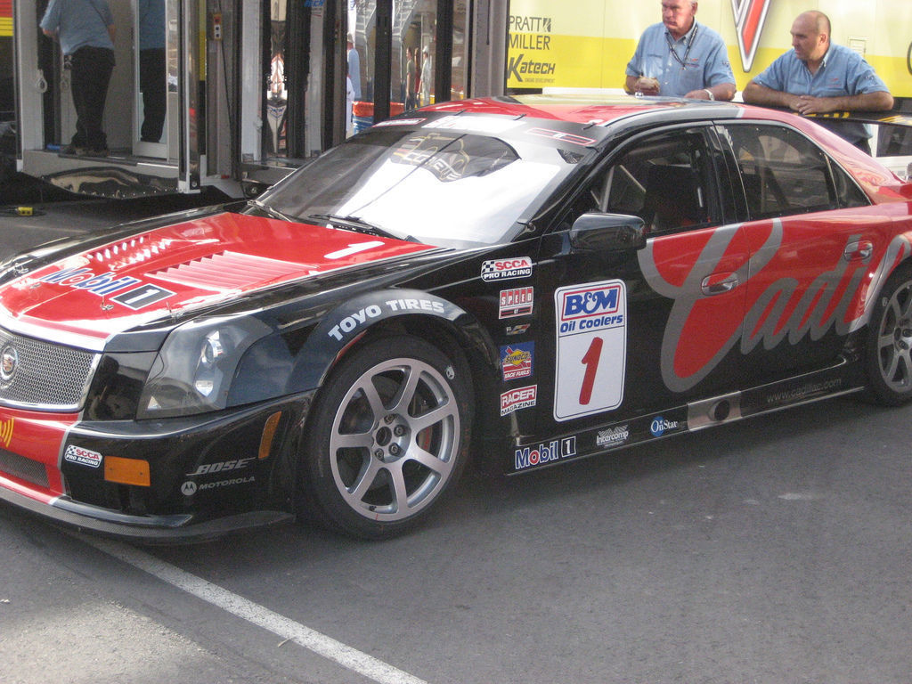 Black and red Cadillac CTS-V race car number 1 with sponsor decals parked beside a transporter