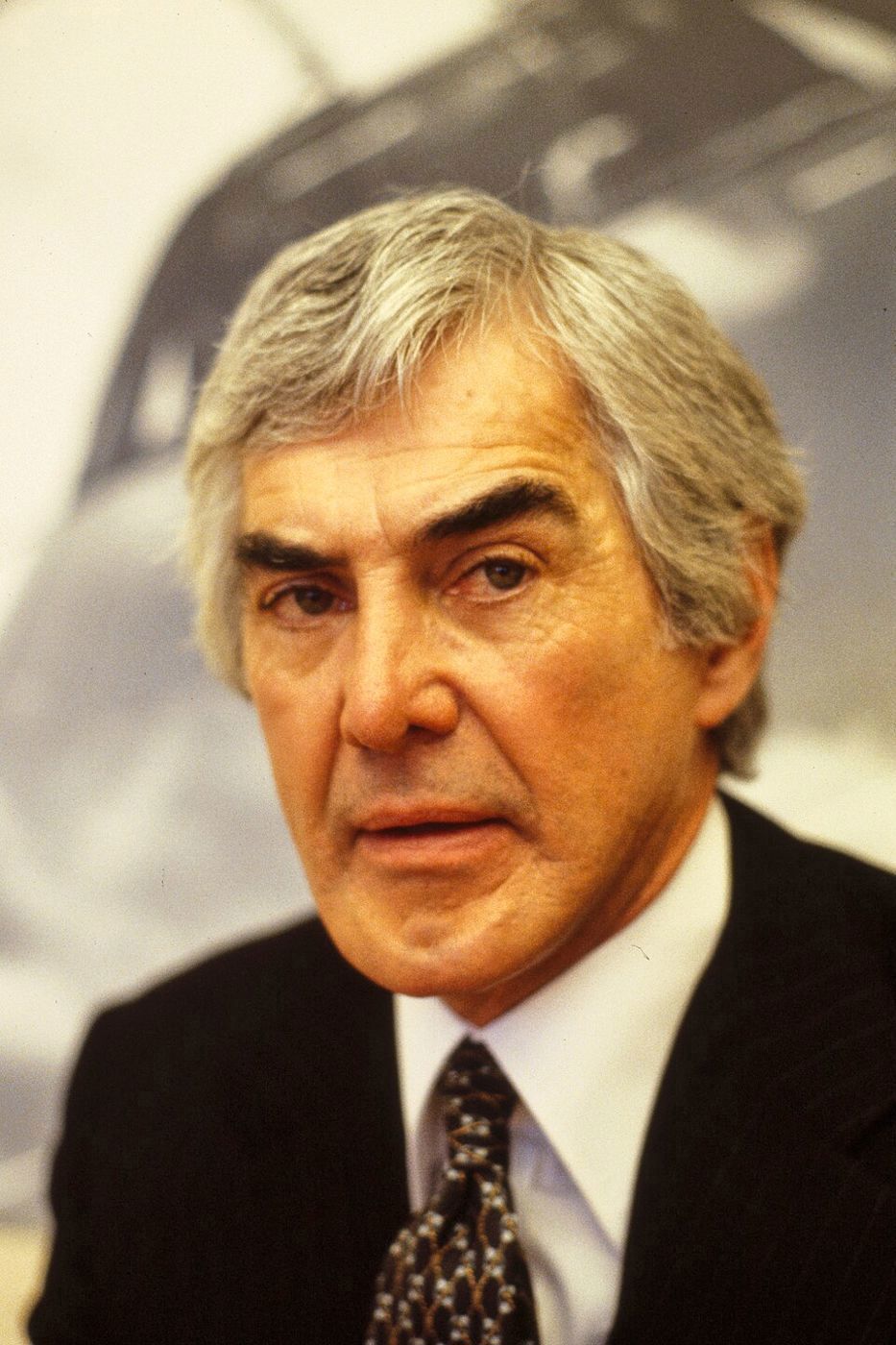 Portrait of John DeLorean with gray hair in a dark pinstripe suit and patterned tie