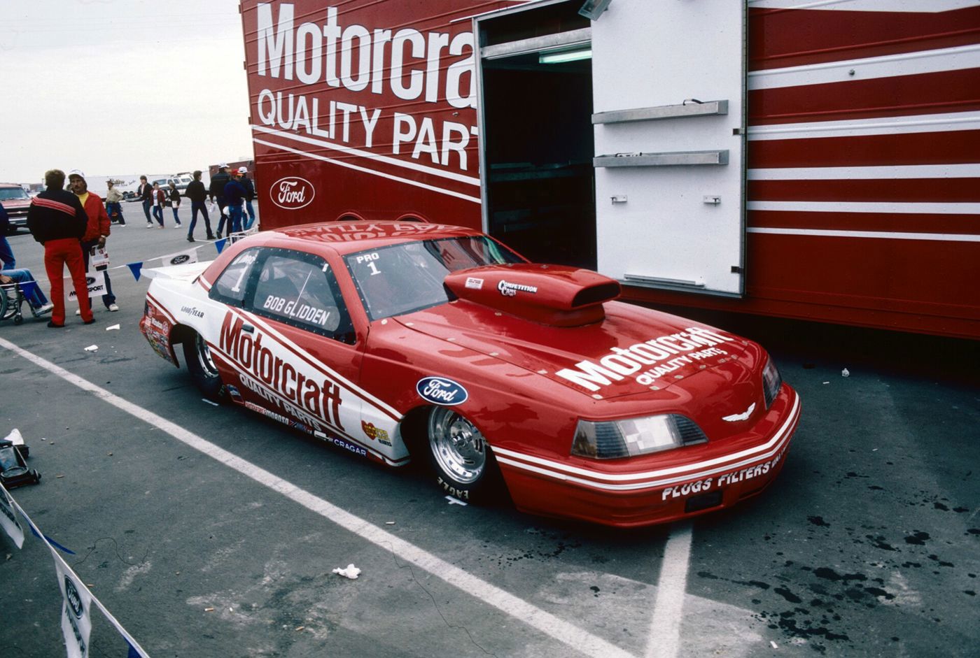 Red and white Motorcraft Ford Thunderbird drag car with Bob Glidden lettering beside its transporter