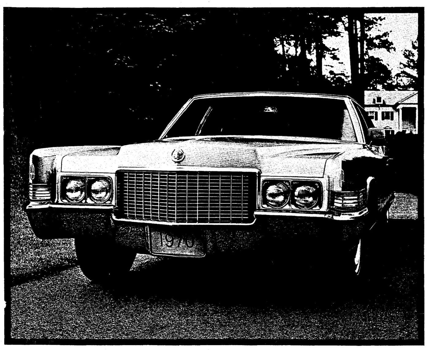 Black-and-white photograph of a light-colored 1970 Cadillac seen head-on on a driveway among trees, with its vertical-bar grille, paired headlamps and a plate reading 1970