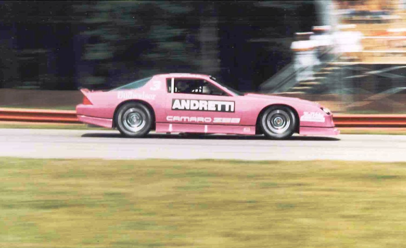 Pink IROC Camaro Z28 race car with ANDRETTI on the door at speed on a road course