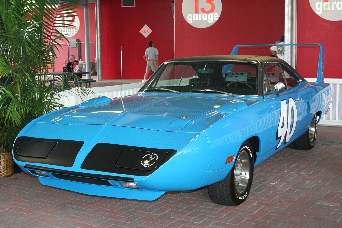 Petty blue 1970 Plymouth Superbird with a black vinyl roof, tall rear wing, nose cone and a large white number 40 on the door, parked on brick pavers in front of red garage walls