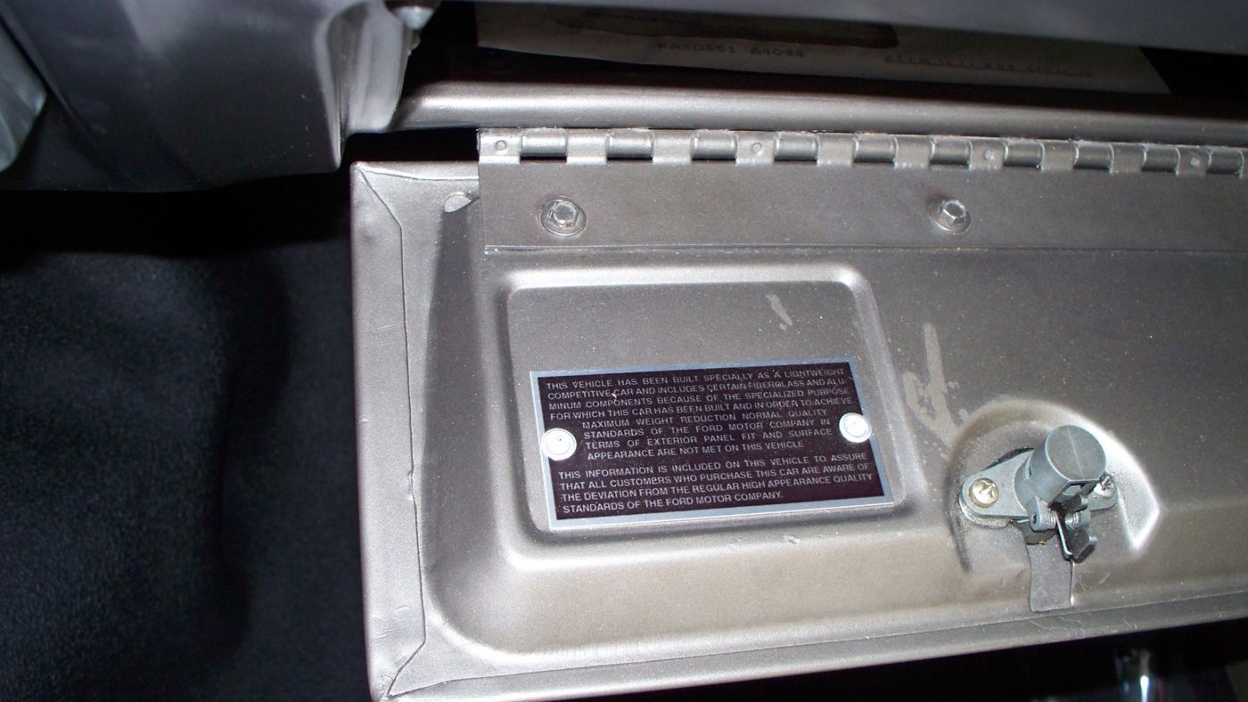 Black plate riveted inside a glovebox door explaining that the car was built as a competitive car with lightweight parts