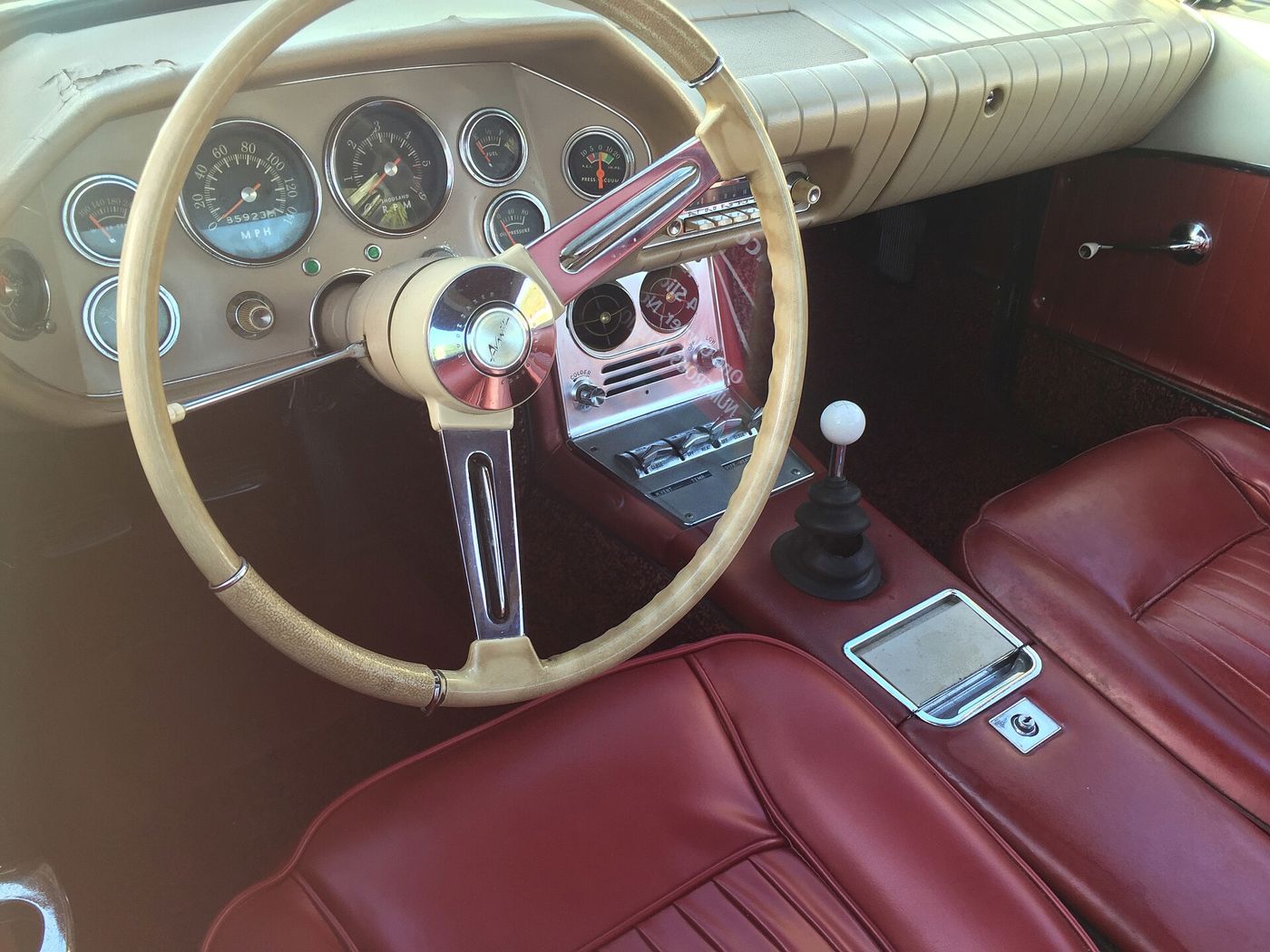 Red leather bucket seats, full instrumentation and the overhead-style center switch console of a 1963 Avanti