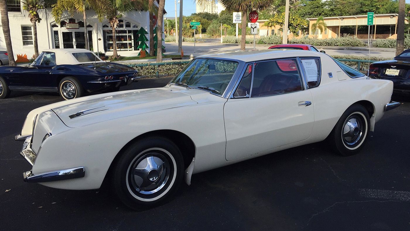 White 1963 Studebaker Avanti with its grille-less nose, wedge profile and hubcaps, parked at a car show